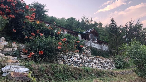 A rustic cabin with a stone foundation, surrounded by lush greenery and flowering plants. - Luxury Private Villa with Mountain View (Banjar)