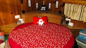 A round bed with a red and white patterned bedspread, a red pillow, and a small stuffed animal on the bed. There is a wooden headboard, a small table with a lamp, and a suitcase on the floor. - Luxury Private Villa with Mountain View (Banjar)