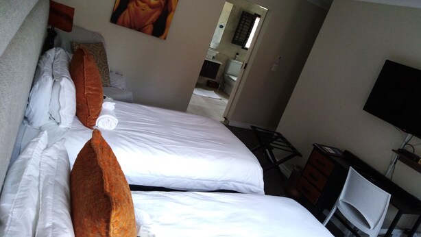 A hotel room with two beds, a TV, a desk, and a bathroom visible through an open door. - Soeteweide North Bb (George)