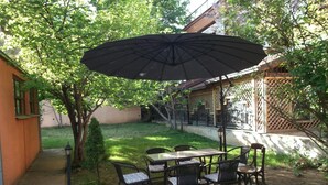 Eine Terrasse im Freien mit Tisch und Stühlen, einem großen Sonnenschirm und einem kleinen Baum.