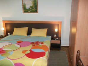 Ein Hotelzimmer mit einem Bett, zwei Nachttischen, einer Lampe, einem Bild an der Wand und einem Holzschrank.