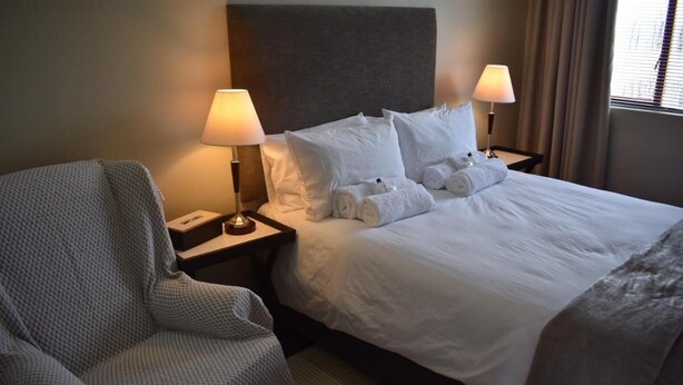 A hotel room with a bed, two bedside lamps, a chair, and a nightstand. - Soeteweide North Bb (George)