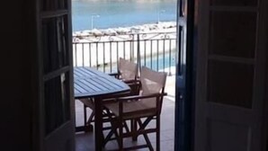 An open door leading to a balcony with a table and chairs, overlooking a coastal area with a fence and greenery. - Villa Yiannoula With Amazing sea View at Skopelos Old Port !!! (Skopelos)
