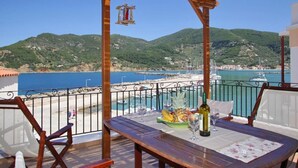 A wooden deck with a table set for dining, overlooking a coastal area with boats and hills. - Villa Yiannoula With Amazing sea View at Skopelos Old Port !!! (Skopelos)
