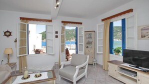 A living room with a TV, a chair, a table with candles, and a view of the sea. - Villa Yiannoula With Amazing sea View at Skopelos Old Port !!! (Skopelos)