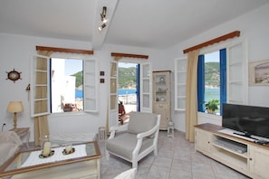 Un salon avec un téléviseur, un fauteuil, une table avec des bougies et une vue sur la mer.