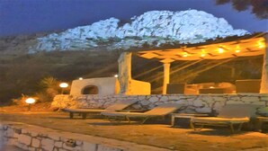 Uma área externa com assentos, paredes de pedra e forno de pedra, com mesas e cadeiras sob luzes de corda.