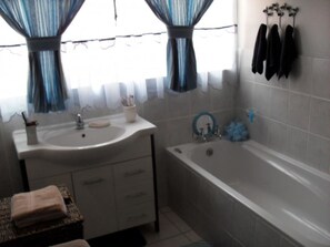 A bathroom with a sink, mirror, and bathtub. There are towels on a chair and a rack with towels on the wall. - Casa Villa Guest House Carletonville - Suite 3 (Merafong City)