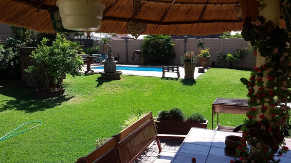 A backyard with a swimming pool, a wooden bench, and various potted plants. - Casa Villa Guest House Carletonville - Suite 3 (Merafong City)