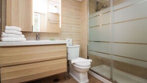 A modern bathroom with a wooden vanity, a toilet, and a glass shower enclosure. - Harbour 374 With Private Roof Terrace in Puerto de Mogan (Mogan)