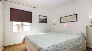 A bedroom with a bed, a window with a blind, a wall-mounted lamp, and a framed picture. - Harbour 374 With Private Roof Terrace in Puerto de Mogan (Mogan)