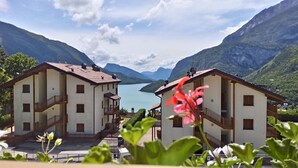 Two white buildings with balconies, a clear view of a lake, and mountains in the background. - Molvenolago Apartment (Molveno)