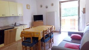 A compact kitchen with a dining table and chairs, a sofa, and a television. - Molvenolago Apartment (Molveno)