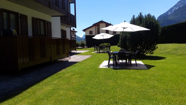 A patio area with outdoor seating and umbrellas, a wooden fence, and a mountain view. - Molvenolago Apartment (Molveno)