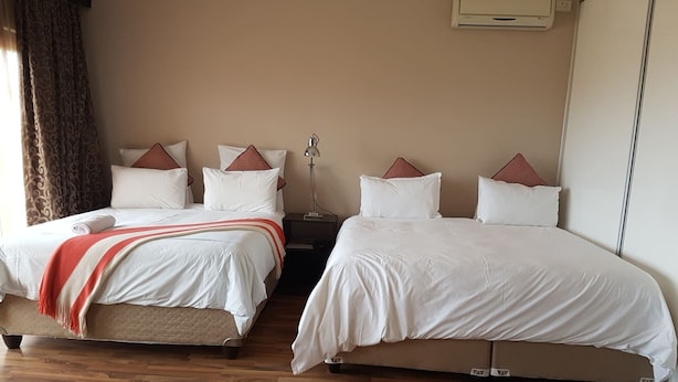 A hotel room with two beds, wooden flooring, and a ceiling air conditioner. - Fairview Bed And Breakfast - Family Room 2 (Umhlanga)