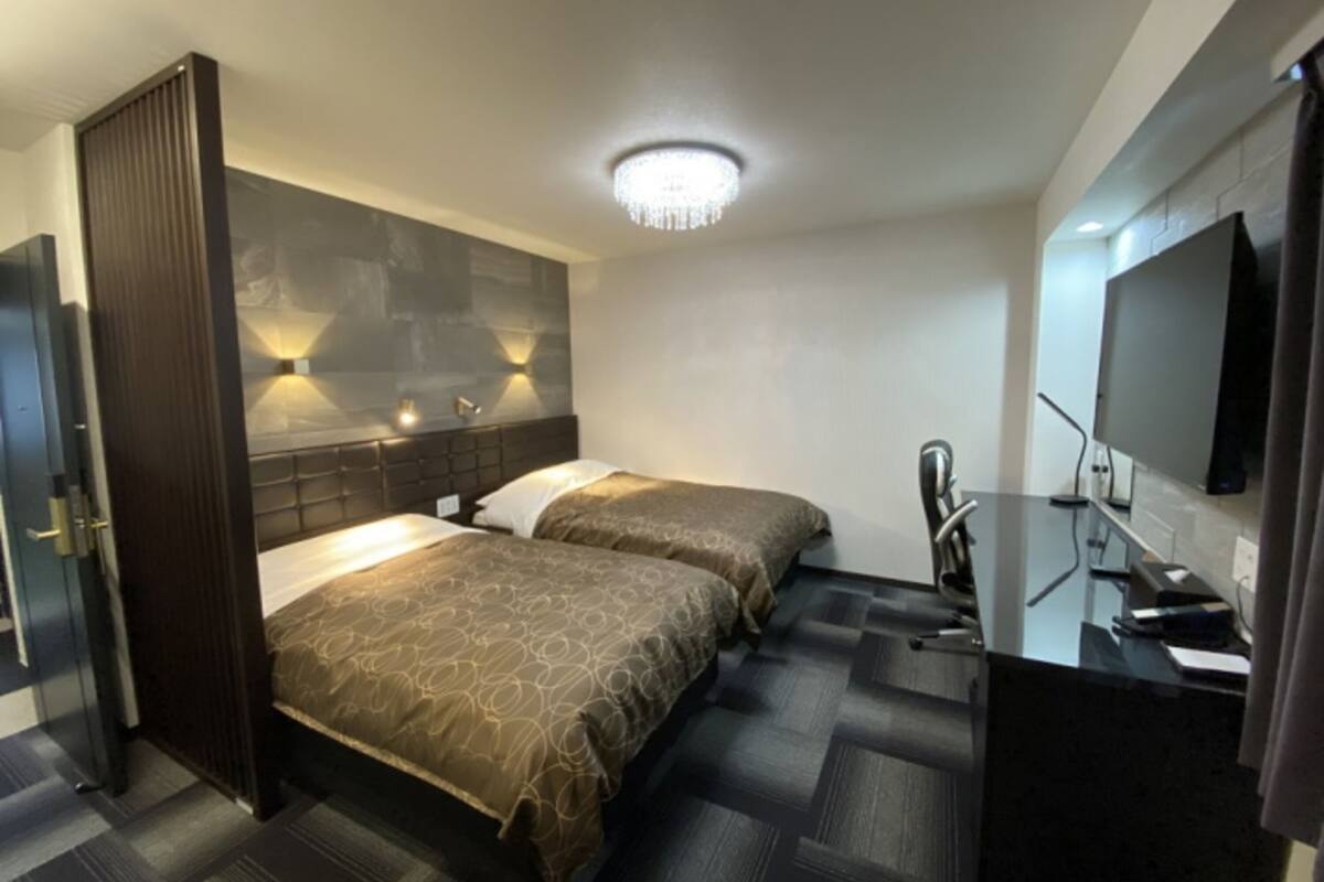 Quarto de hotel com duas camas, uma escrivaninha, televisão e um candelabro.