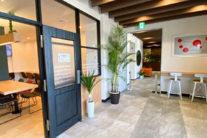 A modern interior with a reception area, a seating area with tables and chairs, and potted plants. - Hotel WIN (Imari)