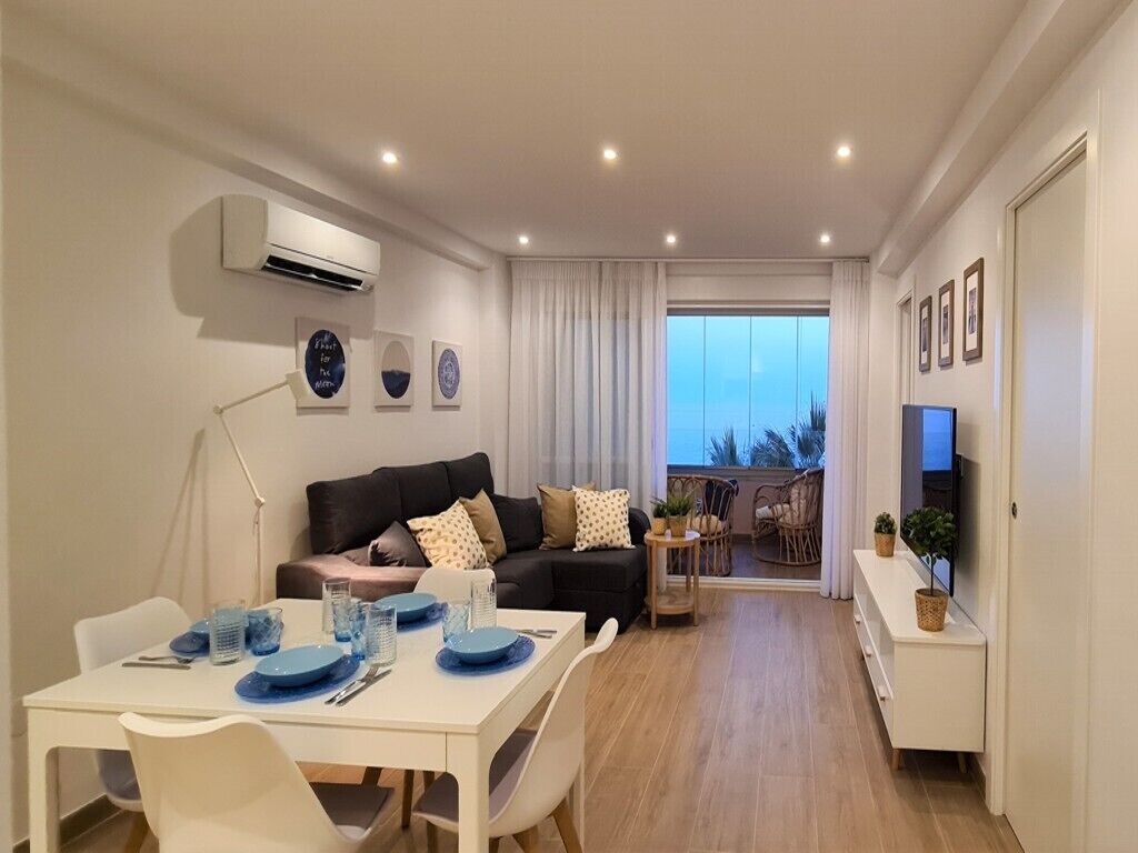 Una sala de estar moderna con comedor, un conjunto de sofás, televisión y un balcón con vistas.