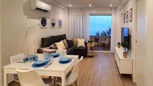 Una sala de estar moderna con comedor, un conjunto de sofás, televisión y un balcón con vistas.