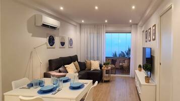 Una sala de estar moderna con comedor, un conjunto de sofás, televisión y un balcón con vistas.