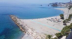 Une plage côtière avec une digue rocheuse, des eaux d’un bleu limpide et une rangée de palmiers.