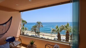 Un balcón con vista al mar, palmeras y coches aparcados.