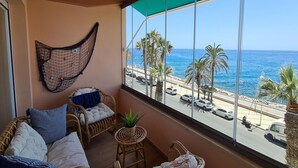 Un balcón con mobiliario de mimbre, una hamaca y vista al mar y a la playa.
