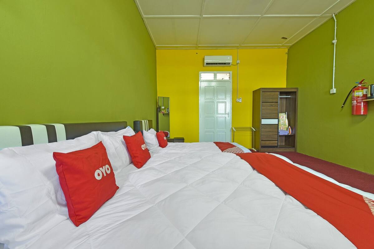 Una camera d'albergo con un letto grande, un armadio, uno specchio e un estintore a parete.