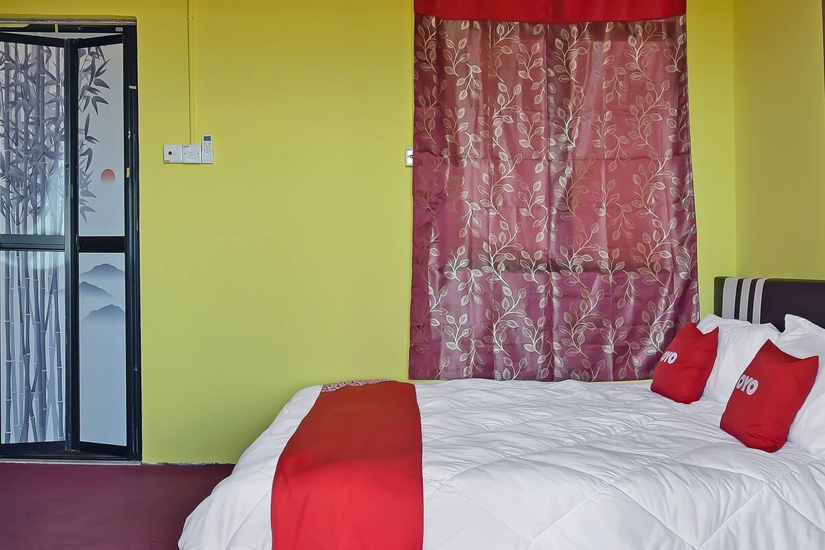 Camera d'albergo con un letto, biancheria rossa e bianca, una coperta rossa e una tenda con motivi floreali.