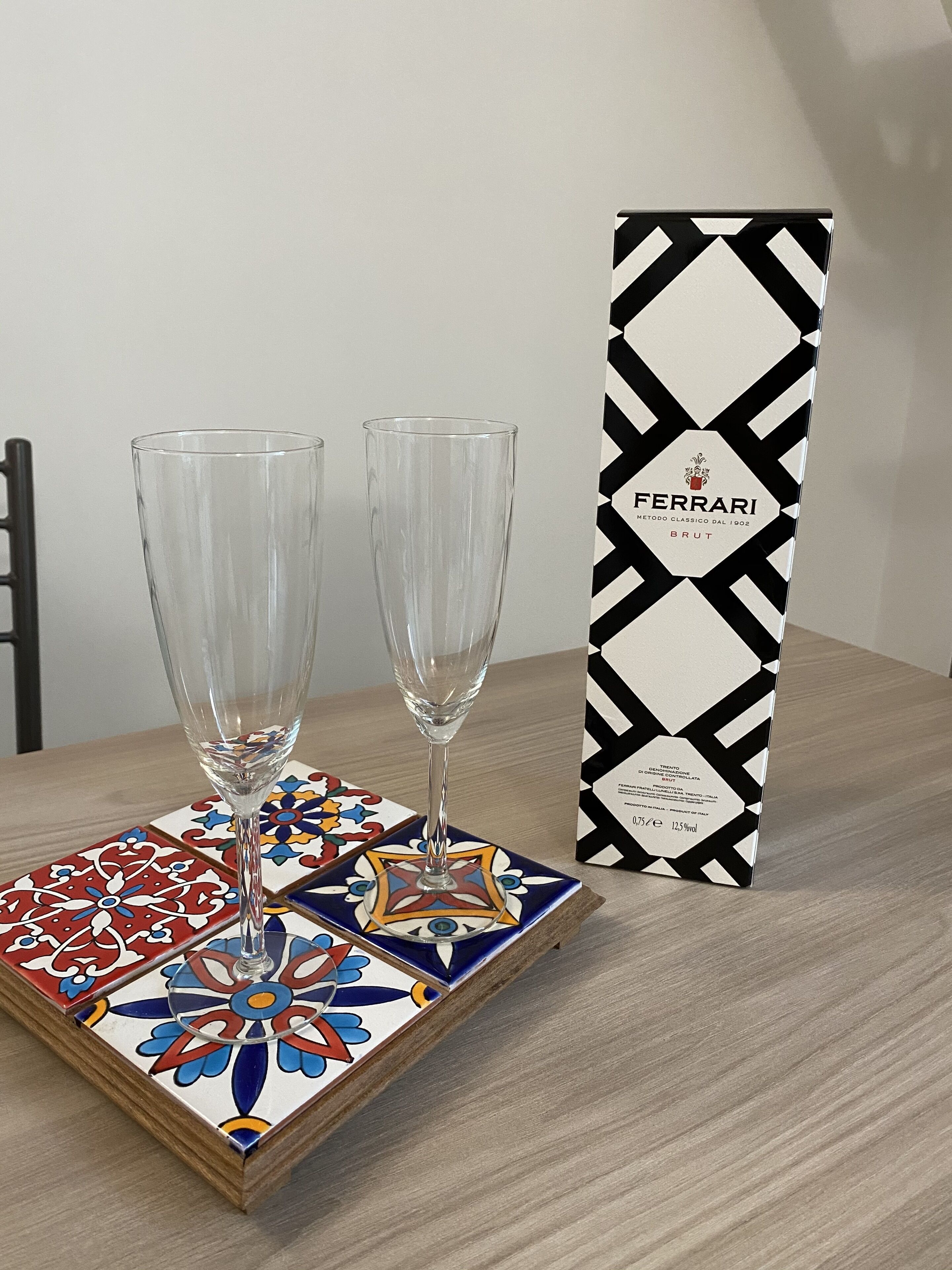 Two empty champagne flutes on a colorful tile, next to a Ferrari Brut wine box.
