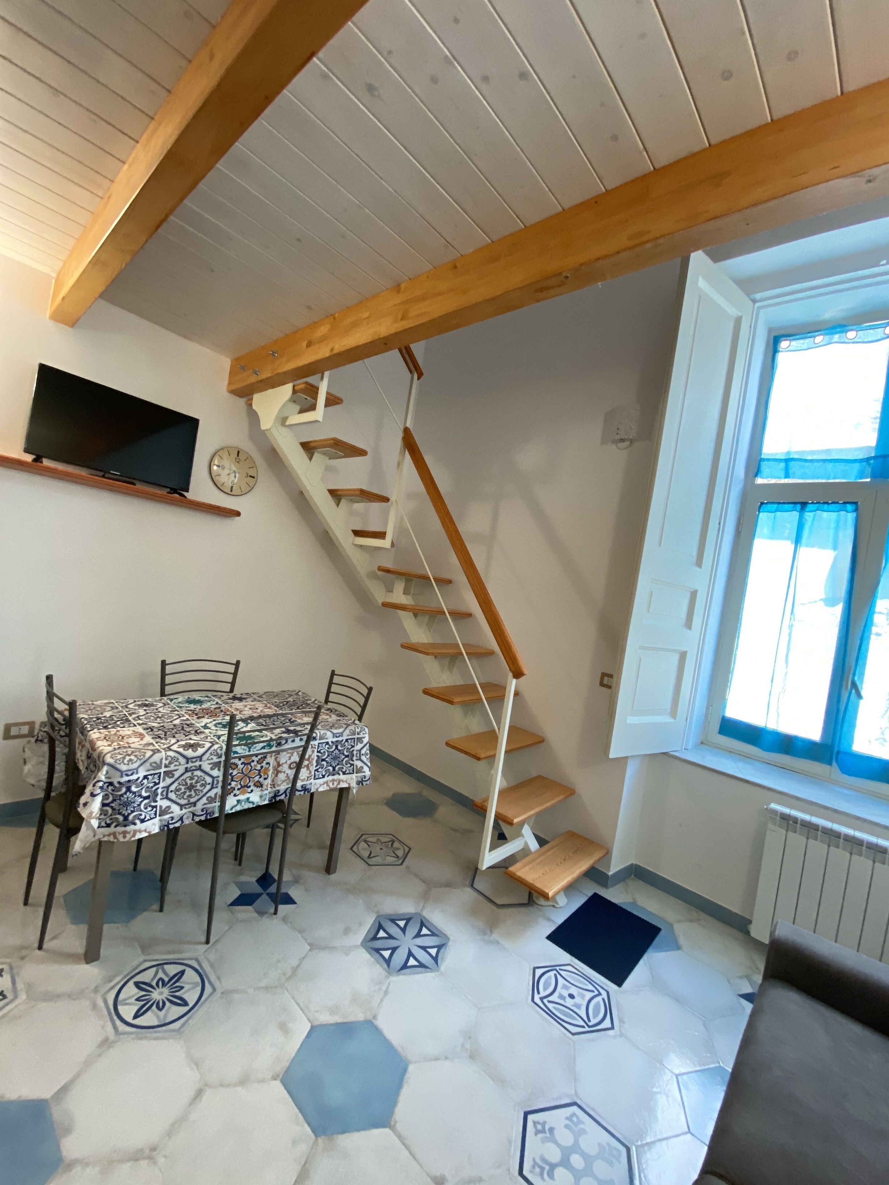 A dining area with a table set for four, a wooden staircase, and a window with curtains.