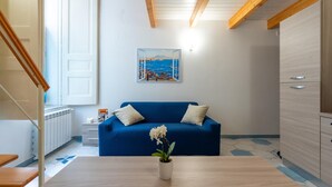 Una sala de estar moderna con un sofá azul, una orquídea blanca sobre una mesa de madera y un cuadro con vistas costeras en la pared.