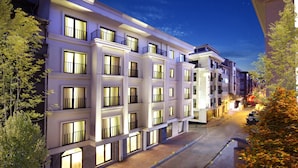 A multi-story hotel with illuminated windows and balconies, a paved street, and trees.