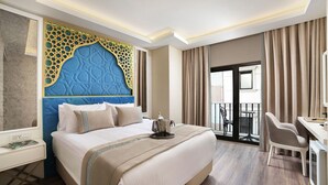 A hotel room with a large bed, a desk, a chair, and a balcony with curtains.
