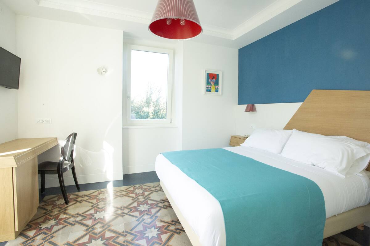 Une chambre d’hôtel avec un lit, un bureau, une chaise et une fenêtre.