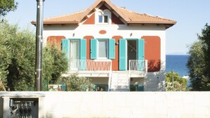 A two-story house with a red-tiled roof, a chimney, and a balcony with blue shutters. - Chiaror di Mare (Gaeta)