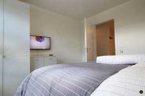 A bedroom with a bed, a television on the wall, and a door leading to another room. - Refugium 7 (Kellenhusen)