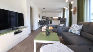 En moderne stue med et fladskærms-TV, en sofa, et sofabord og en vase med blomster.