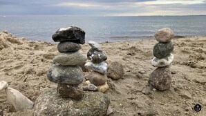 En bunke sten på en sandstrand med udsigt til havet og en overskyet himmel.