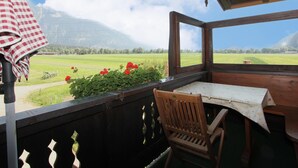 Un balcon en bois avec une table et une chaise, donnant sur un champ verdoyant et des montagnes.