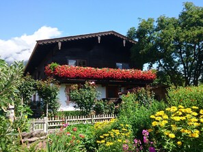 Ein traditionelles Chalet mit einem Balkon, der in rotes Blumenbeet getaucht ist, umgeben von einer Vielfalt bunter Gartenblumen.