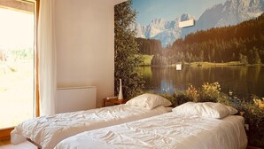 Un dormitorio con dos camas, un ventanal grande y un mural de un lago de montaña.