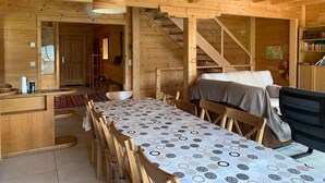 Interior de una cabaña de madera con comedor, escalera y estantería.