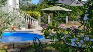 Une piscine entourée de verdure, un espace extérieur aménagé avec des sièges et un escalier menant à un bâtiment.