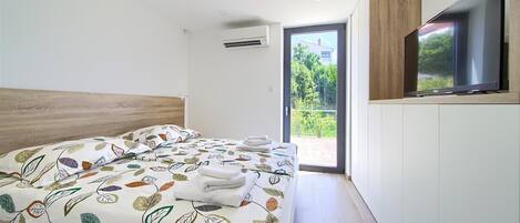 A modern bedroom with a large bed, a television mounted on the wall, and a sliding glass door leading to a balcony.