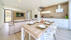 A modern kitchen with a wooden island, white cabinetry, and a dining area with white chairs.