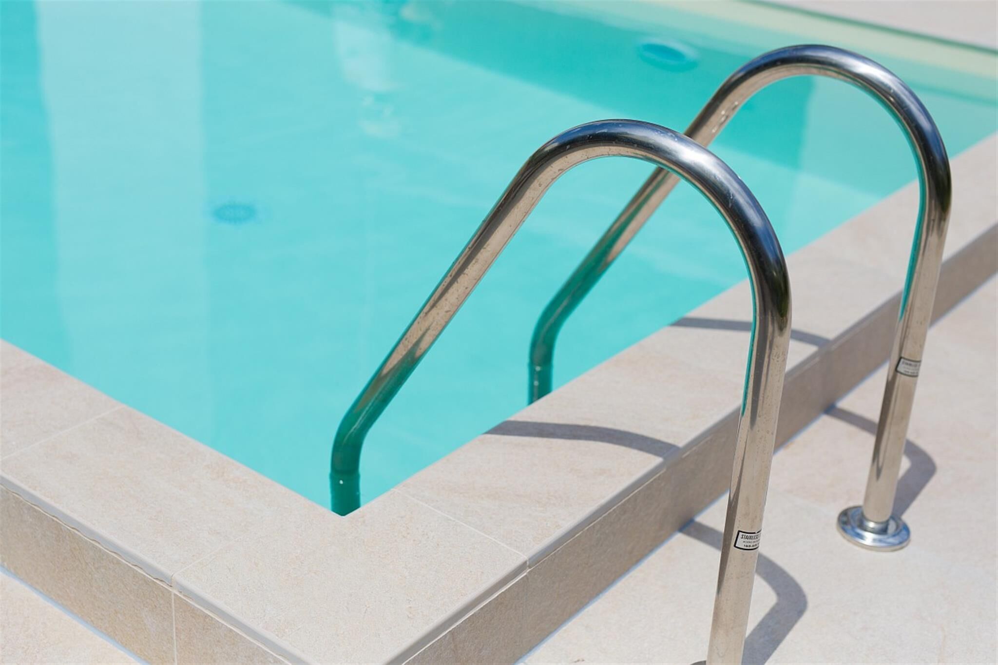 A swimming pool with metal handrails and tiled edges.