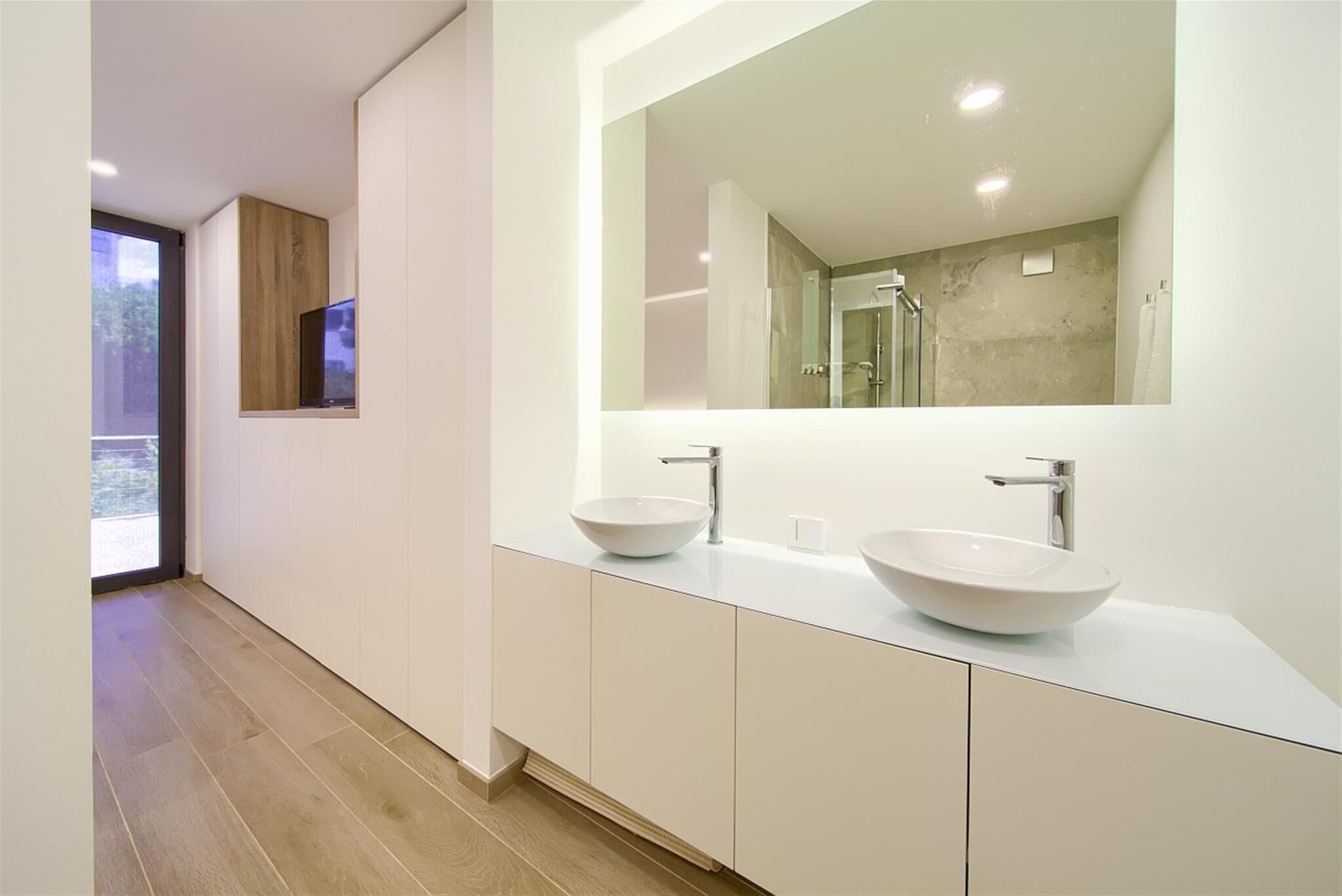 A modern bathroom with two large white sinks, a large mirror, and a glass shower enclosure.