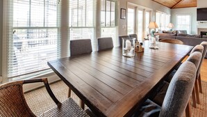 Een eetgedeelte met een houten tafel, stoelen en uitzicht door grote ramen.