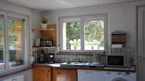 Una cocina compacta con armarios de madera, lavadora, microondas y ventana con vista a árboles.